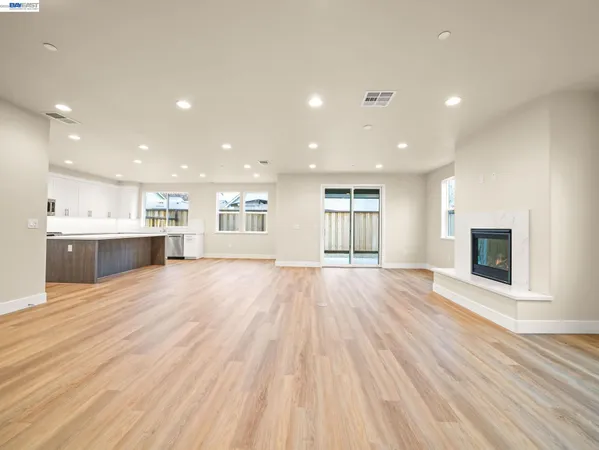 a view of an empty room with wooden floor and a kitchen
