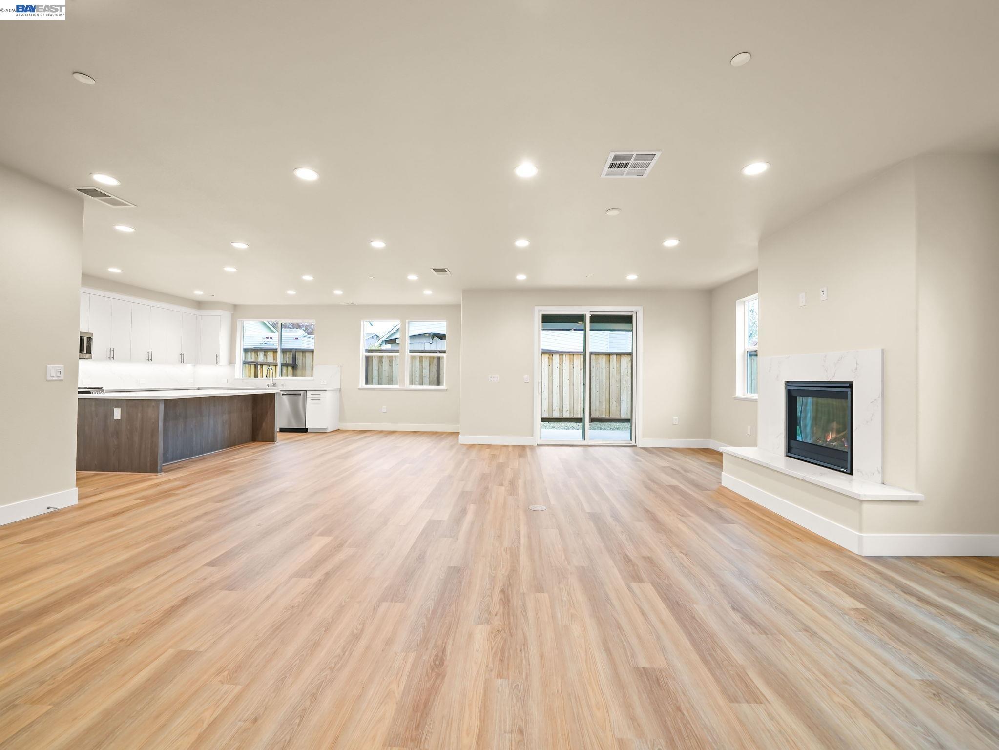 a view of an empty room with wooden floor and a kitchen