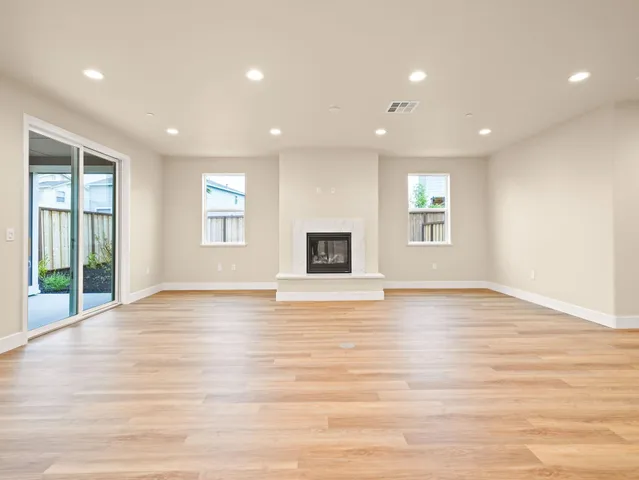 a view of an empty room with wooden floor and kitchen
