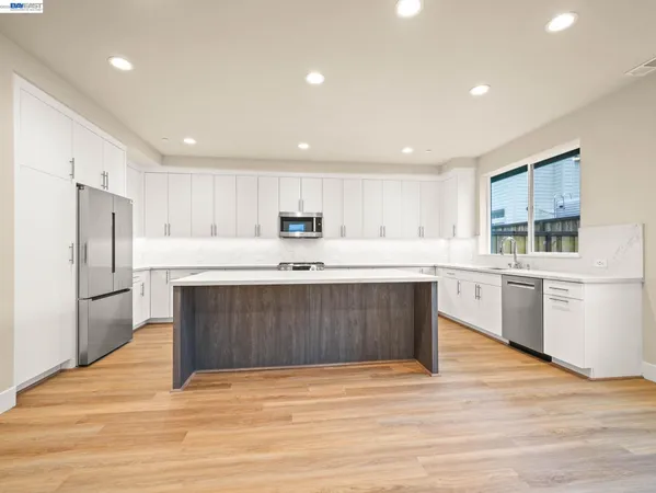 a kitchen with stainless steel appliances kitchen island granite countertop a refrigerator sink and white cabinets