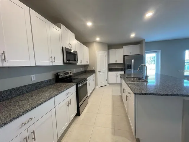 a large kitchen with granite countertop a stove a sink a microwave a counter top space and cabinets