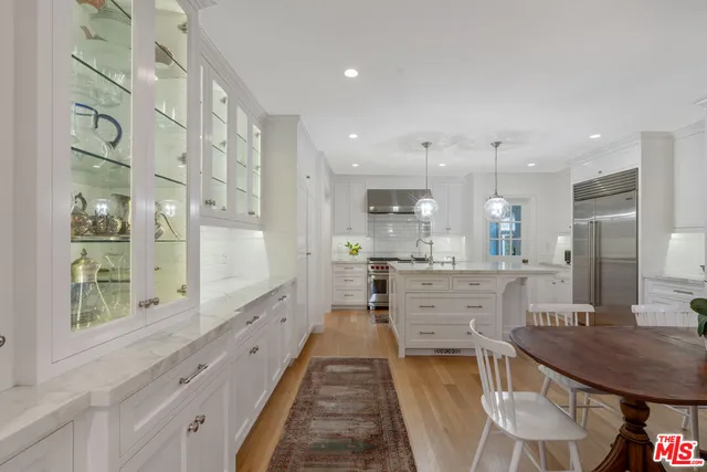a large white kitchen with kitchen island a large counter space a sink stainless steel appliances and cabinets