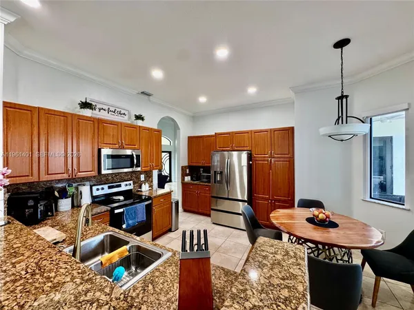 a kitchen with stainless steel appliances granite countertop a stove a refrigerator a sink a dining table and chairs with wooden floor
