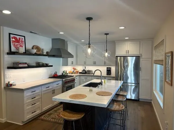 a kitchen with stainless steel appliances kitchen island granite countertop a sink a stove a refrigerator and island with wooden floor