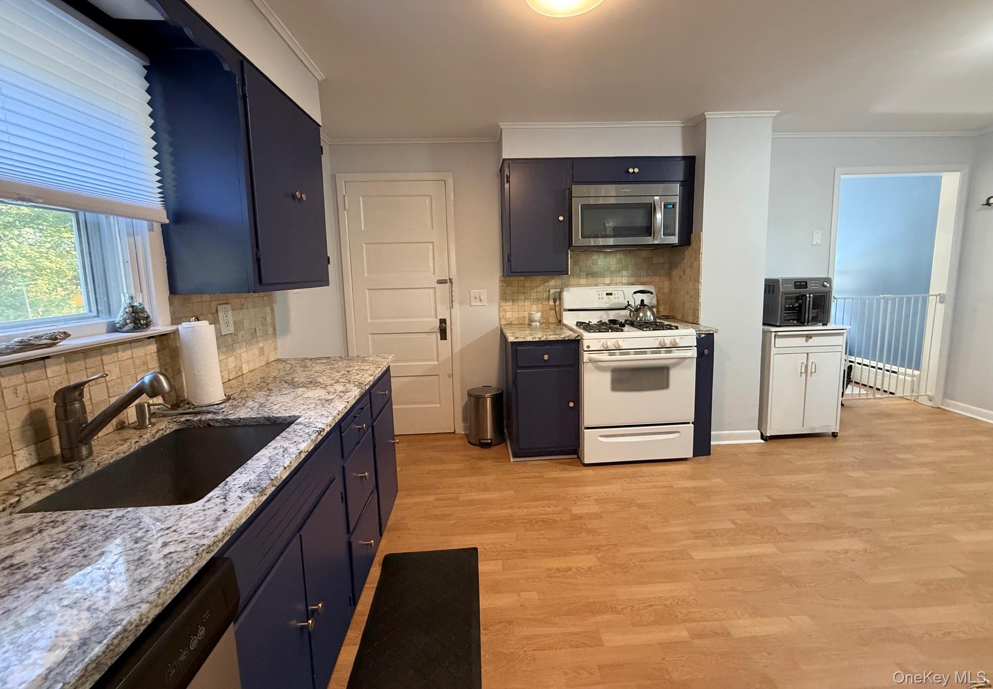 25 School Street Port Washington, NY 11050 - Photo 23 of 25 Kitchen featuring tasteful backsplash, stainless steel appliances, crown molding, light wood-type flooring, and light stone countertops