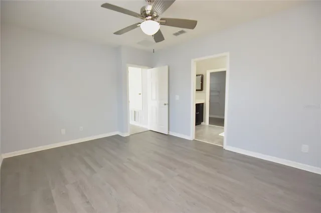 an empty room with wooden floor ceiling fan and window