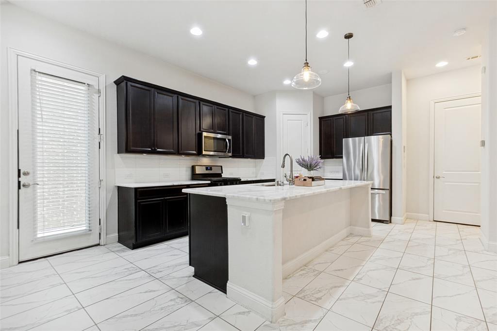 605 Ansley Way Allen, TX 75013 - Photo 14 of 28 Kitchen featuring a central island with a stone countertop, dark wood-finish cabinetry, stainless steel appliances, and large format tile flooring