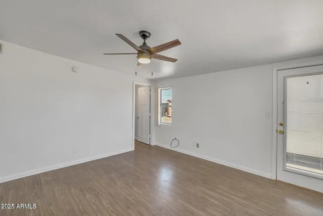 an empty room with wooden floor ceiling fan and windows