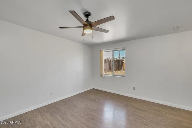 an empty room with wooden floor ceiling fan and window