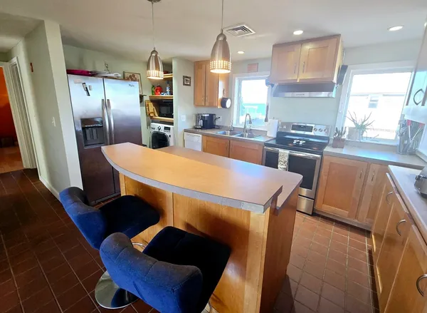 a kitchen with stainless steel appliances kitchen island granite countertop a refrigerator a stove a sink and a dining table with wooden floor