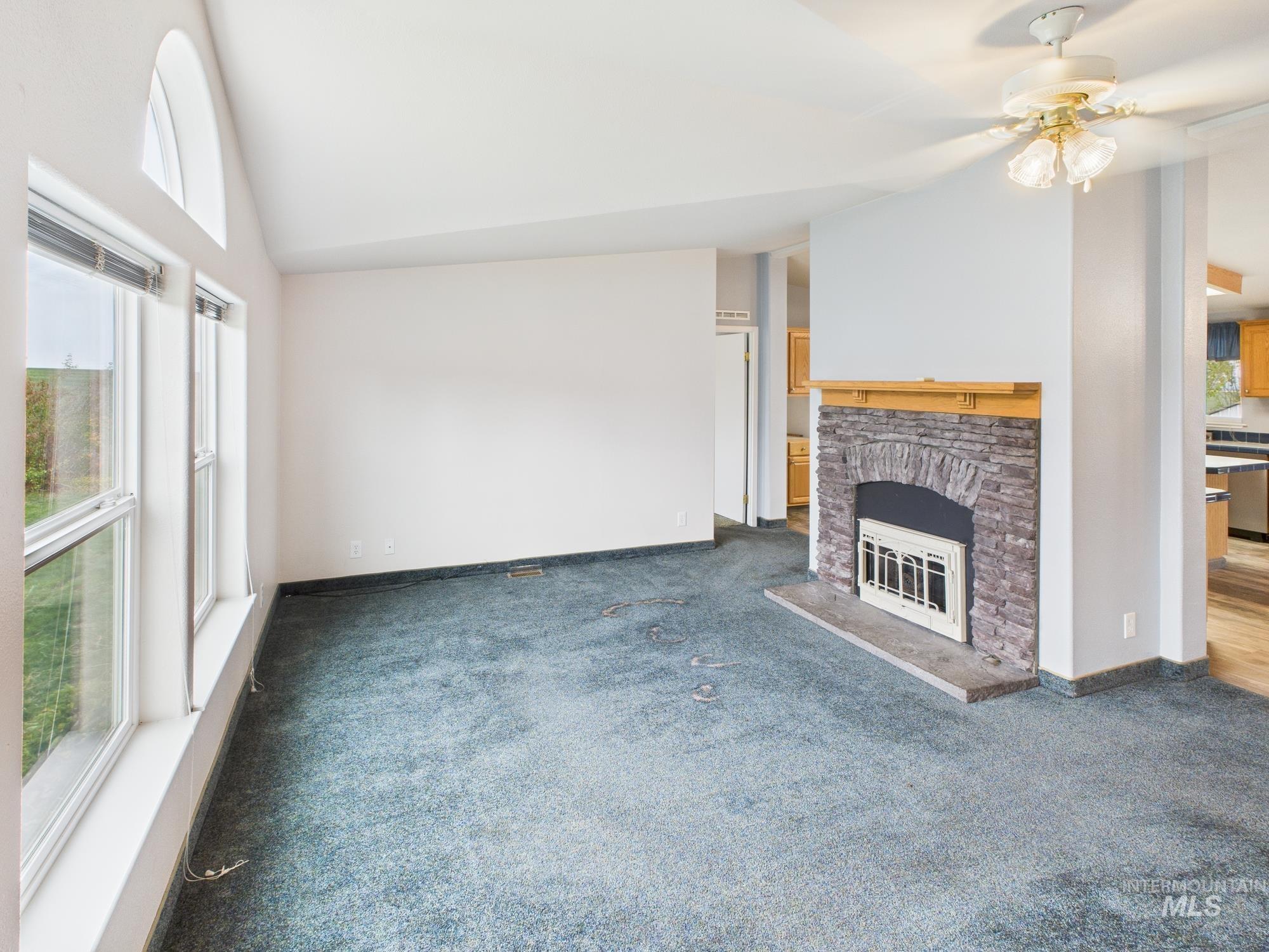 523 3rd Street Ferdinand, ID 83526 - Photo 4 of 41 Unfurnished living room with vaulted ceiling, a stone fireplace, carpet, and a ceiling fan