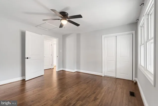 an empty room with wooden floor fan and windows