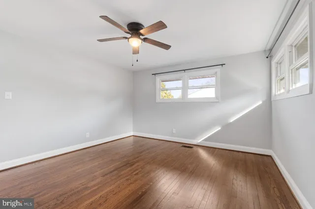 an empty room with wooden floor fan and windows