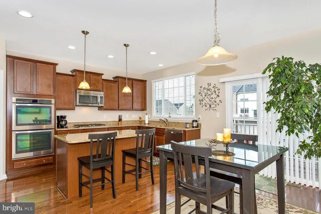 a kitchen with stainless steel appliances granite countertop a stove refrigerator a dining table and chairs with wooden floor