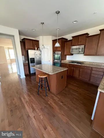 a room with stainless steel appliances kitchen island granite countertop a stove a sink a refrigerator and chairs