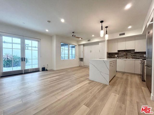 a large white kitchen with kitchen island a stove a refrigerator cabinets and wooden floor