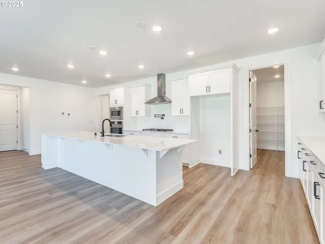 a large kitchen with kitchen island a sink a stove a refrigerator and white cabinets with wooden floor