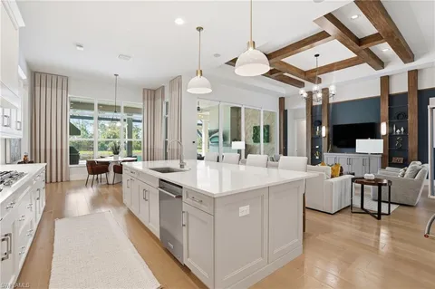 a large white kitchen with a large island a stove a sink a refrigerator and a fireplace