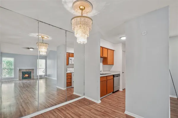 an empty room with wooden floor chandeliers and kitchen view