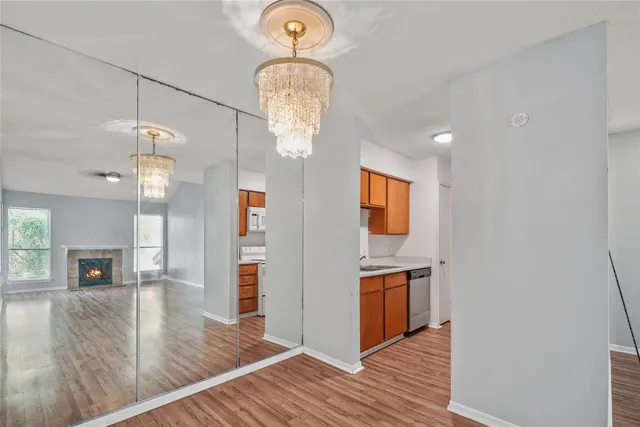 an empty room with wooden floor chandeliers and kitchen view