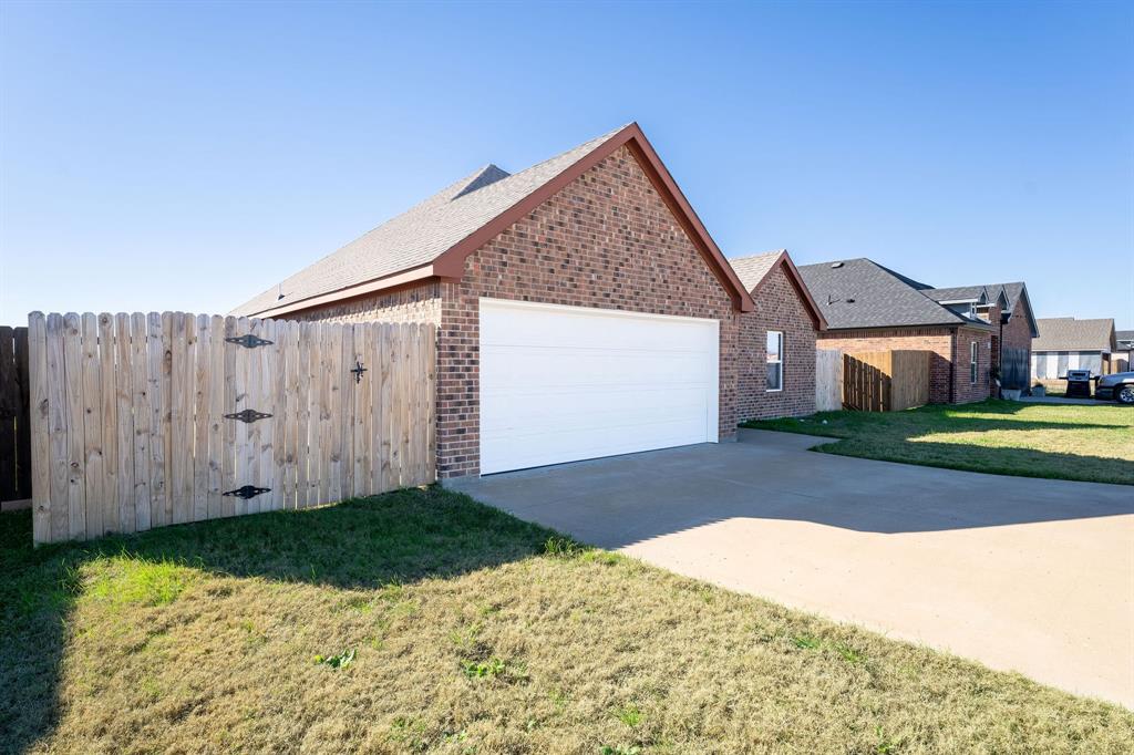 1020 Springview Lane Mabank, TX 75147 - Photo 3 of 15 View of side of home featuring a gate, an attached garage, concrete driveway, and brick siding