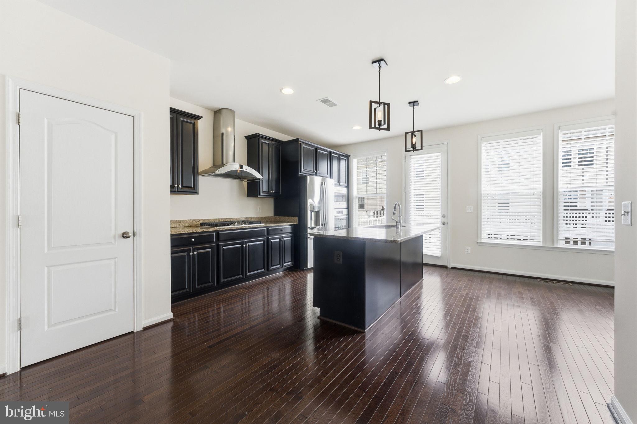 42396 Benfold Square Brambleton, VA 20148 - Photo 11 of 65 a kitchen with stainless steel appliances kitchen island wooden floors stove and white cabinets