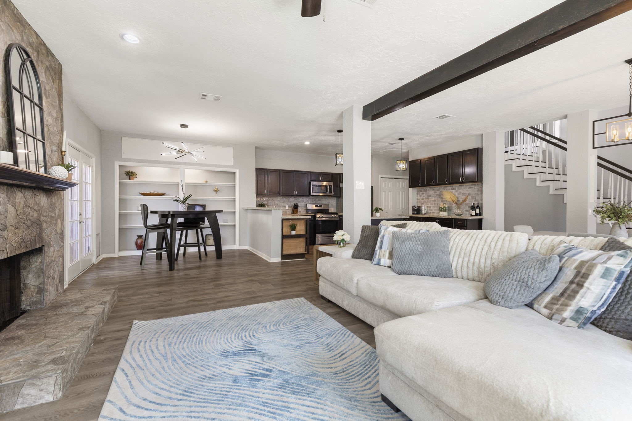 2110 Paso Rello Drive Houston, TX 77077 - Photo 11 of 41 This inviting open-concept living space features a cozy stone fireplace and elegant dark wood kitchen cabinets. The room is enhanced by modern lighting fixtures and a natural flow to the dining area and staircase.