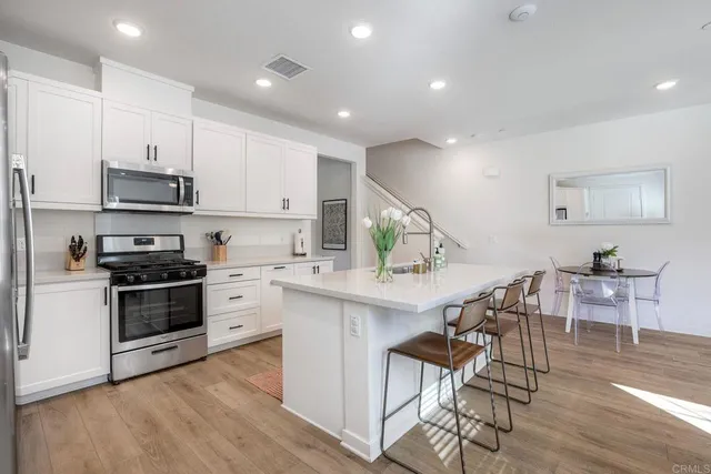 a kitchen with stainless steel appliances kitchen island a table chairs in it and white cabinets