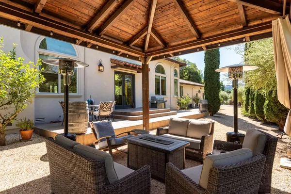 a view of a patio with couches table and chairs under an umbrella with a large tree