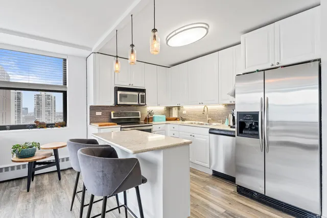 a kitchen with stainless steel appliances granite countertop a refrigerator a stove top oven a sink dishwasher and white cabinets with wooden floor