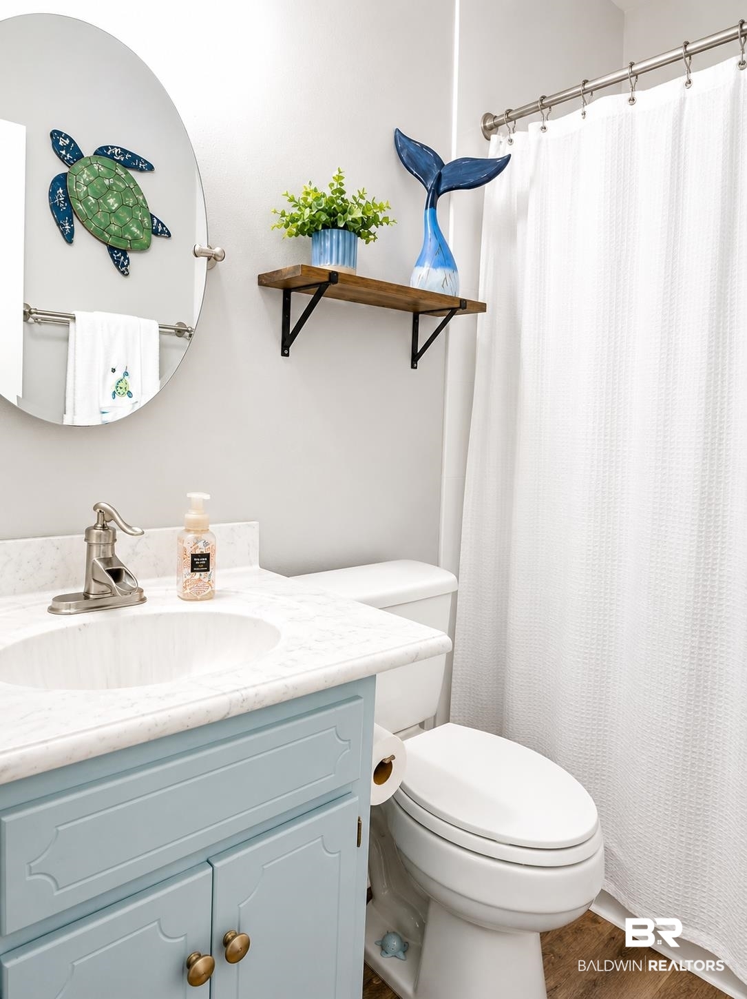 21733 Sedlack Road Silverhill, AL 36576 - Photo 20 of 22 Bathroom featuring a light blue vanity with brass hardware, a white countertop, an oval-shaped mirror, and wood-finish flooring
