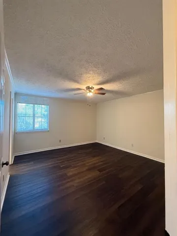 an empty room with wooden floor chandelier fan and windows