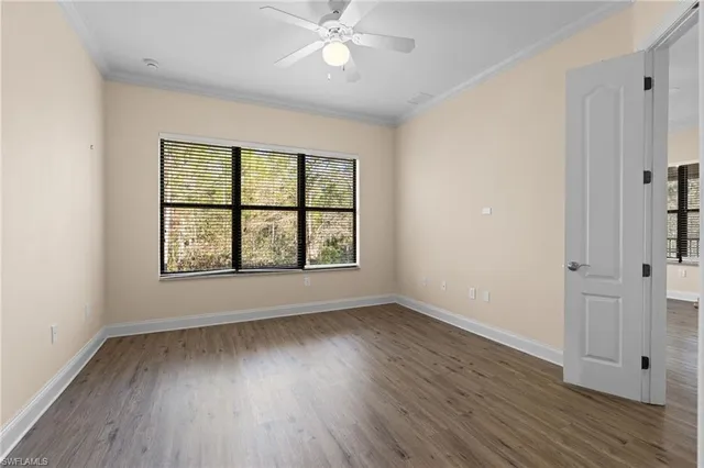 an empty room with wooden floor chandelier fan and windows