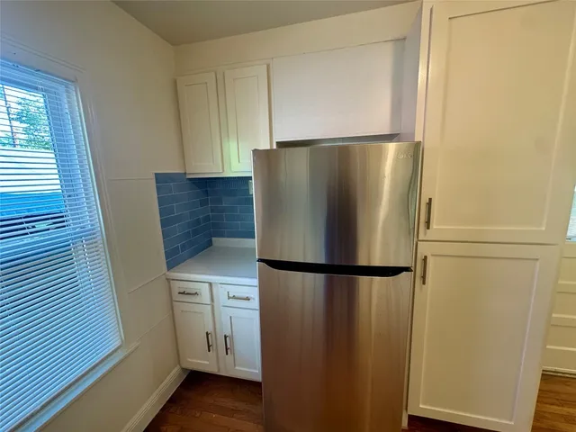 a view of a refrigerator in kitchen and an empty room with wooden floor