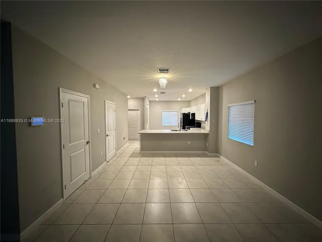 a view of an empty room and kitchen space with windows