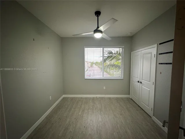 an empty room with wooden floor ceiling fan and windows