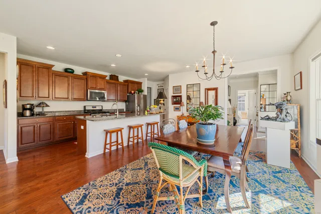 a kitchen with stainless steel appliances kitchen island granite countertop a refrigerator a stove a kitchen island a dining table and chairs with wooden floor