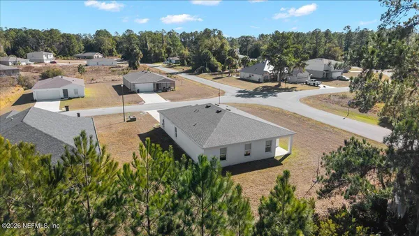 an aerial view of a house with yard and trees in the background