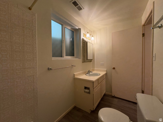 595 Meadowlark Road Orem, UT 84097 - Photo 61 of 87 Bathroom featuring a single vanity with an integrated sink, wood-finish flooring, a window with frosted panes, and a tiled shower surround