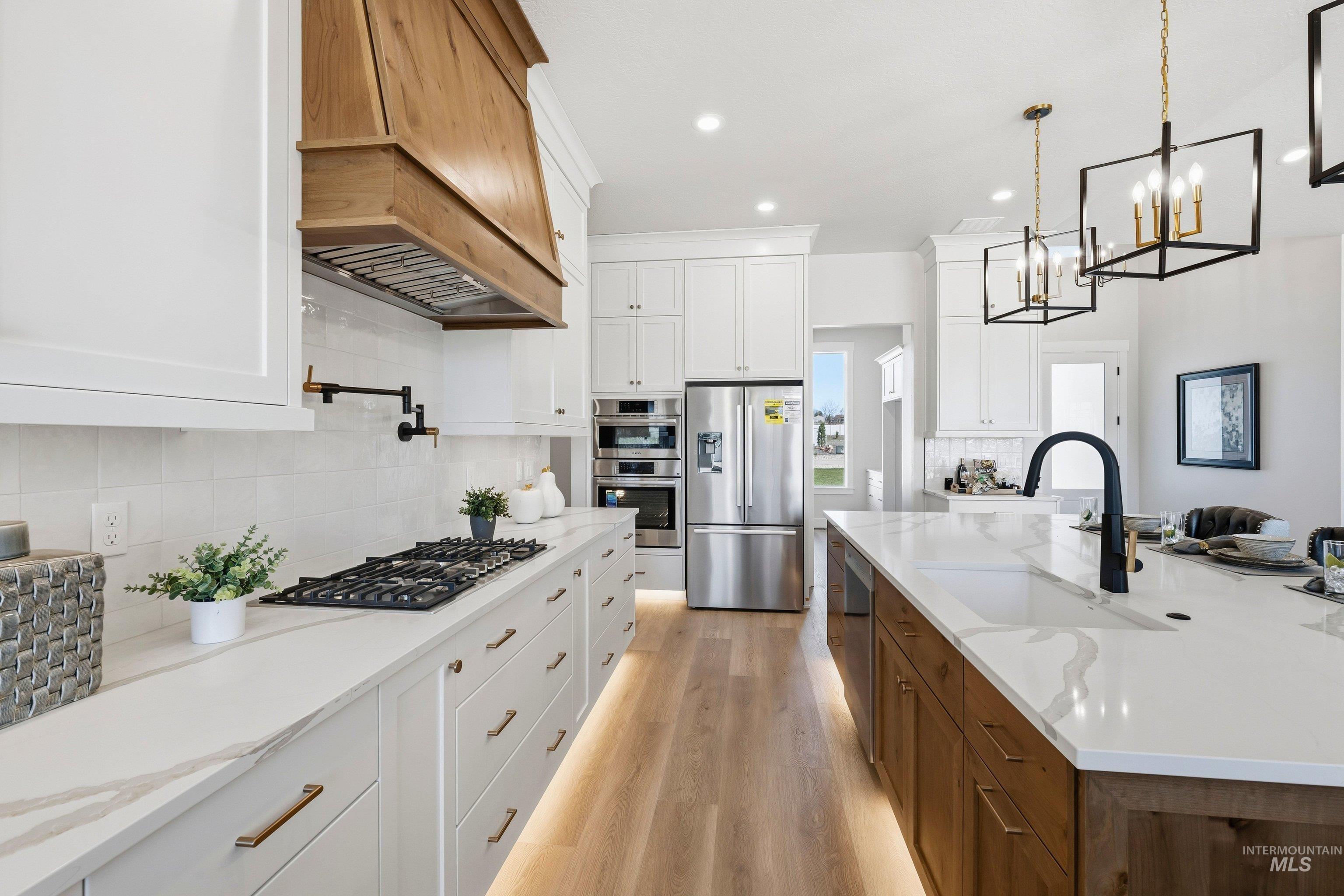 24897 Ardmore Court Caldwell, ID 83607 - Photo 12 of 47 Kitchen with dual tone cabinetry, light stone counters, stainless steel appliances, light wood-style flooring, and a spacious island