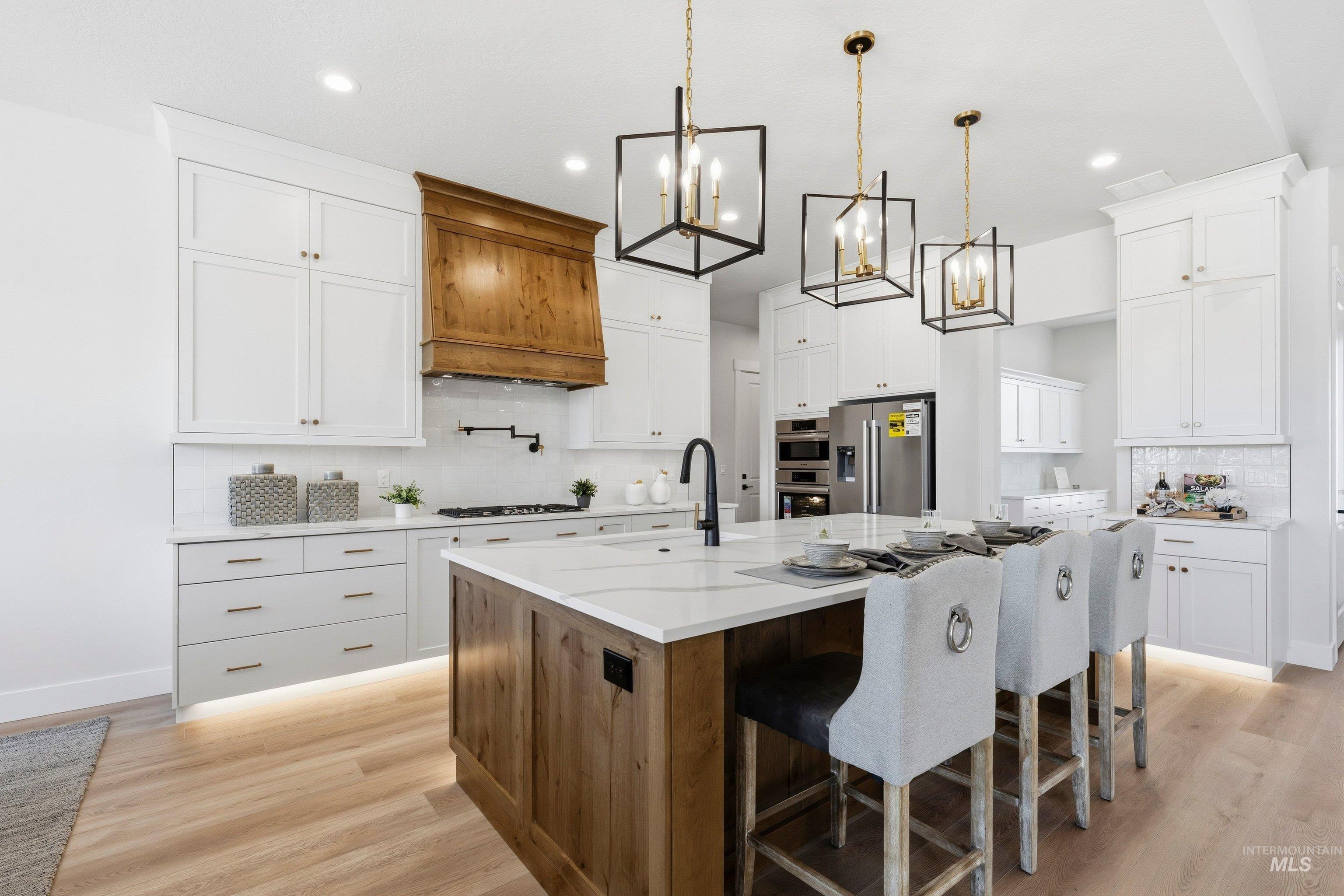 24897 Ardmore Court Caldwell, ID 83607 - Photo 13 of 47 Dual tone kitchen featuring backsplash, dual tone cabinets, a kitchen breakfast bar, a center island with sink, and light wood-type flooring