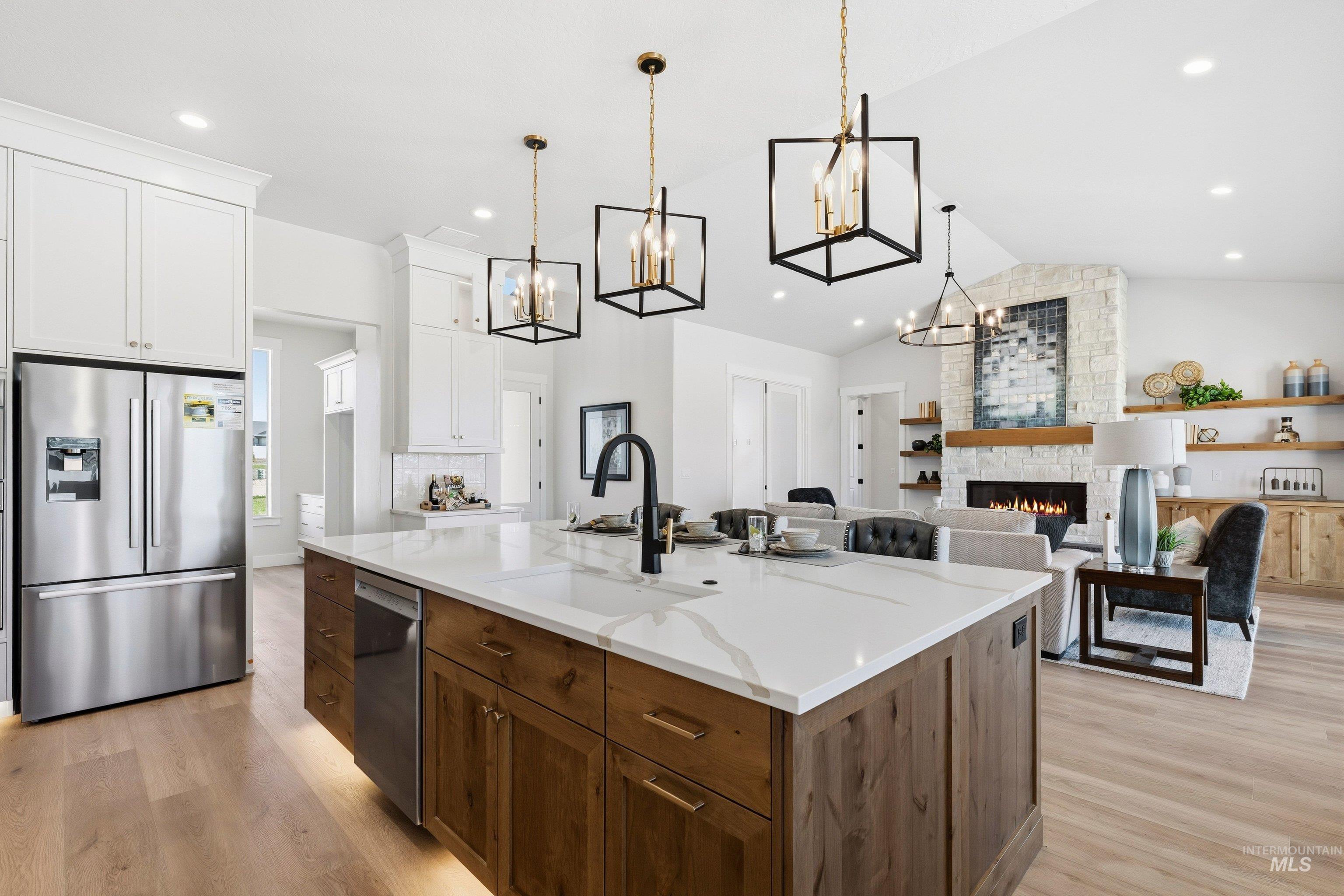 24897 Ardmore Court Caldwell, ID 83607 - Photo 44 of 47 Dual tone kitchen with dual tone cabinets, stainless steel appliances, a stone fireplace, open floor plan, and a center island with sink