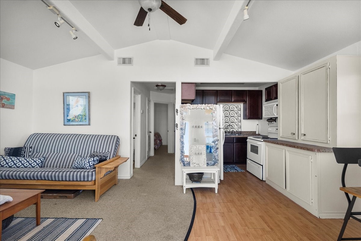 819 Seashell Drive Surfside Beach, TX 77541 - Photo 14 of 27 This cozy living space features an open layout with a vaulted ceiling, combining a compact kitchen with warm cabinetry and an adjacent living area. The living room includes a striped sofa/futon and a wooden coffee table, complemented by light walls and a ceiling fan, creating a welcoming atmosphere.