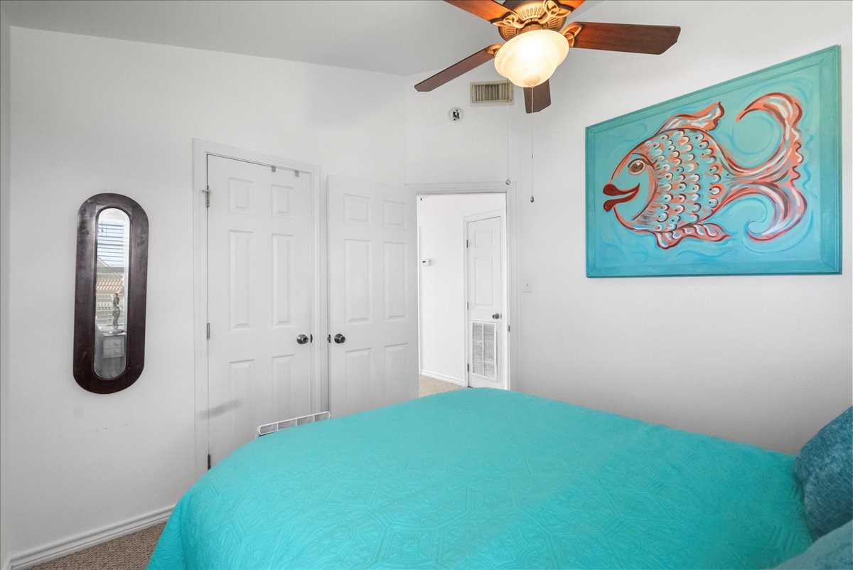 819 Seashell Drive Surfside Beach, TX 77541 - Photo 16 of 36 This bedroom features a ceiling fan, white walls, and a vibrant fish artwork. It includes two doors and a wall mirror, with a turquoise bedspread adding a pop of color.