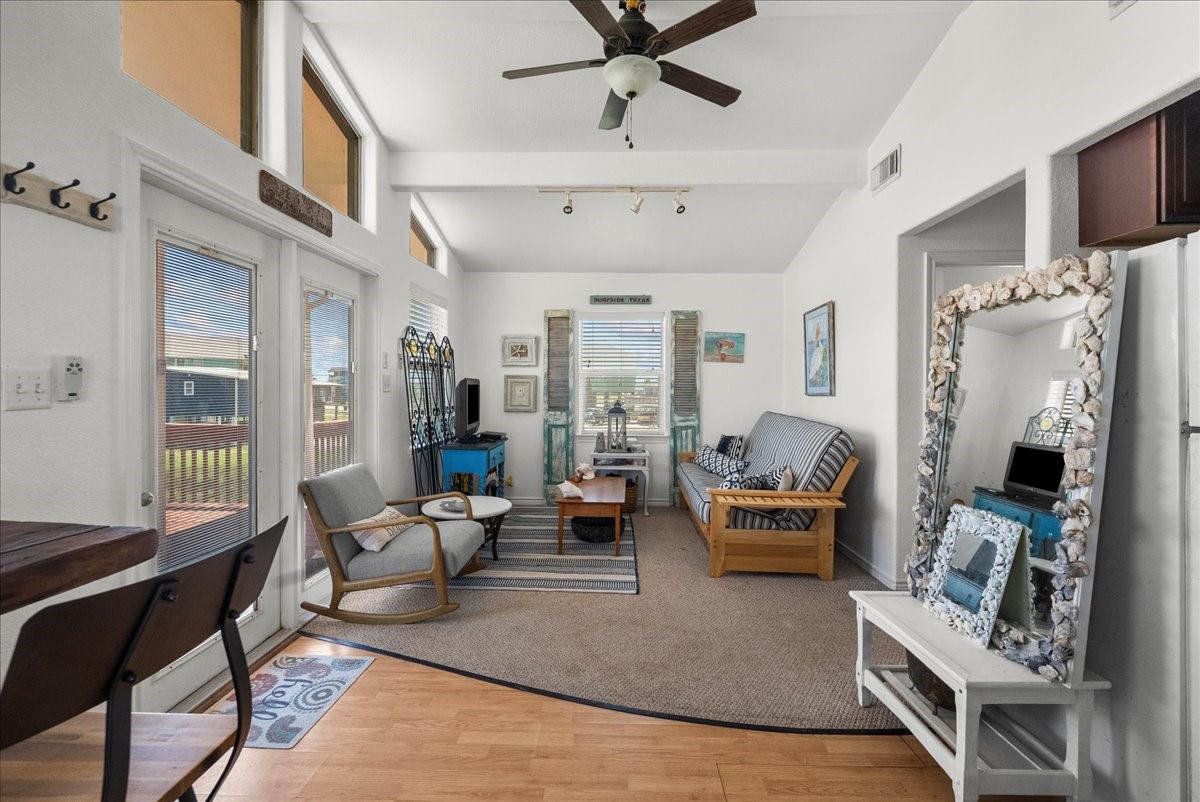 819 Seashell Drive Surfside Beach, TX 77541 - Photo 17 of 27 Bright living room with high ceilings, featuring large windows and a ceiling fan. The space is furnished with a comfortable futon, chairs, and a decorative mirror. Access to a deck is available through glass doors, offering plenty of natural light.