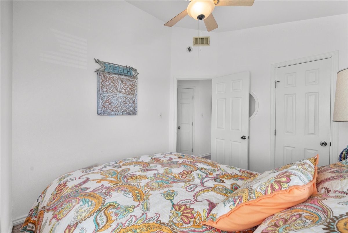 819 Seashell Drive Surfside Beach, TX 77541 - Photo 19 of 36 Cozy bedroom with bright, colorful bedding and a ceiling fan. The room features white walls, two doors, and a beach-themed wall decoration, creating a relaxed, inviting atmosphere.