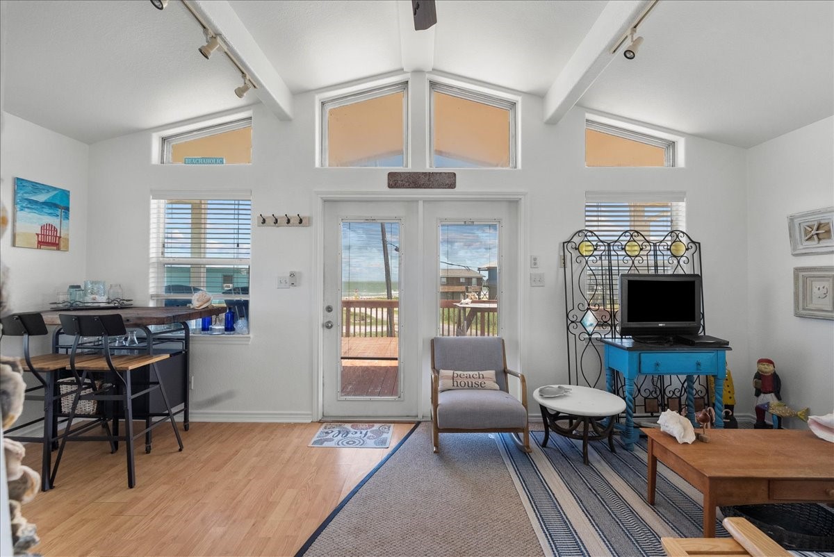 819 Seashell Drive Surfside Beach, TX 77541 - Photo 24 of 36 This bright living area features high ceilings, large windows, and a door leading to a deck with ocean views. It includes a cozy seating area, a small dining table, and a decorative corner with a TV stand. The space has a beachy, relaxed vibe with light wood floors and nautical decor.