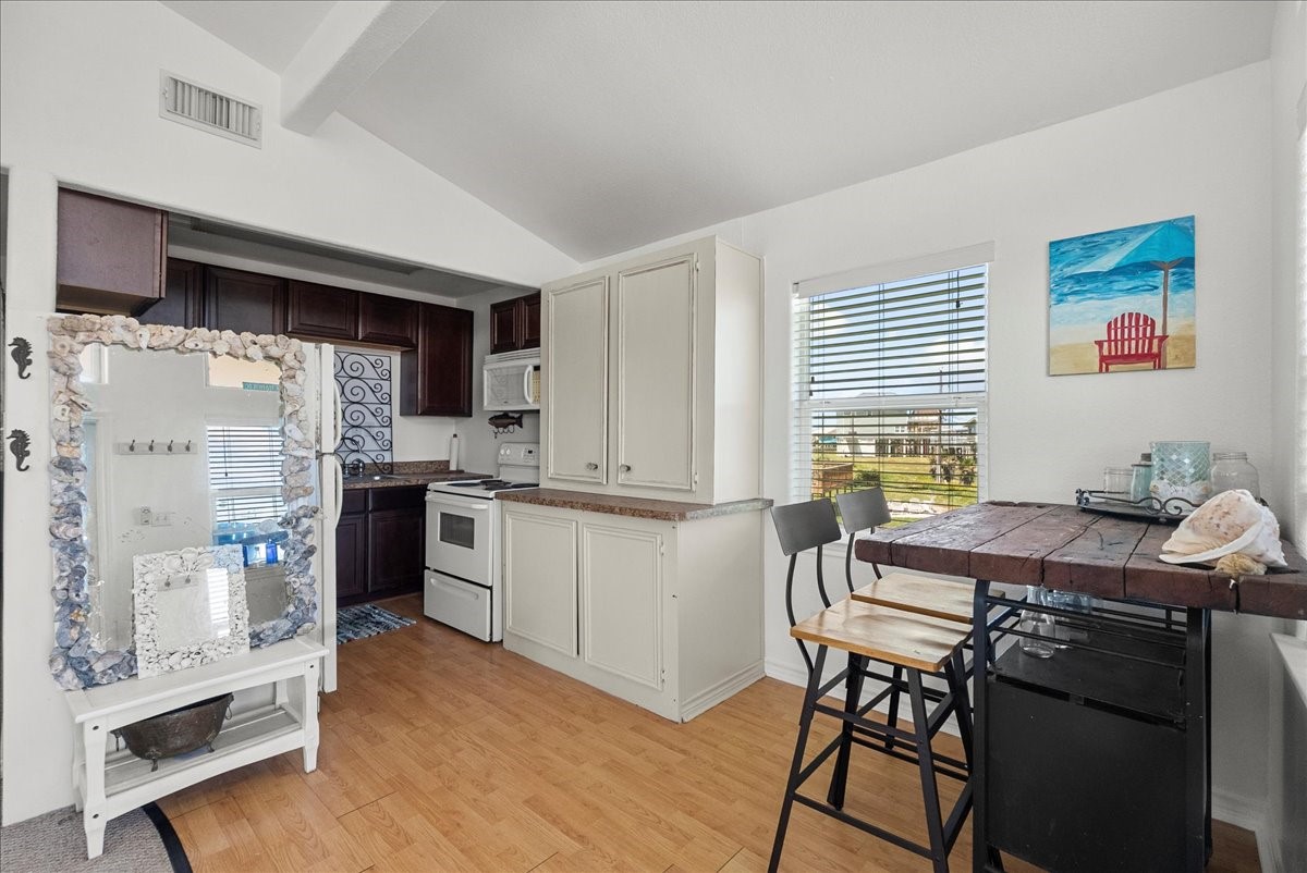 819 Seashell Drive Surfside Beach, TX 77541 - Photo 27 of 36 This cozy kitchen features a mix of dark and light cabinetry, a small dining area with a wooden table and stools, and a large window allowing natural light to brighten the space. The decor includes a beach-themed painting and a shell-framed mirror, adding a charming coastal vibe.