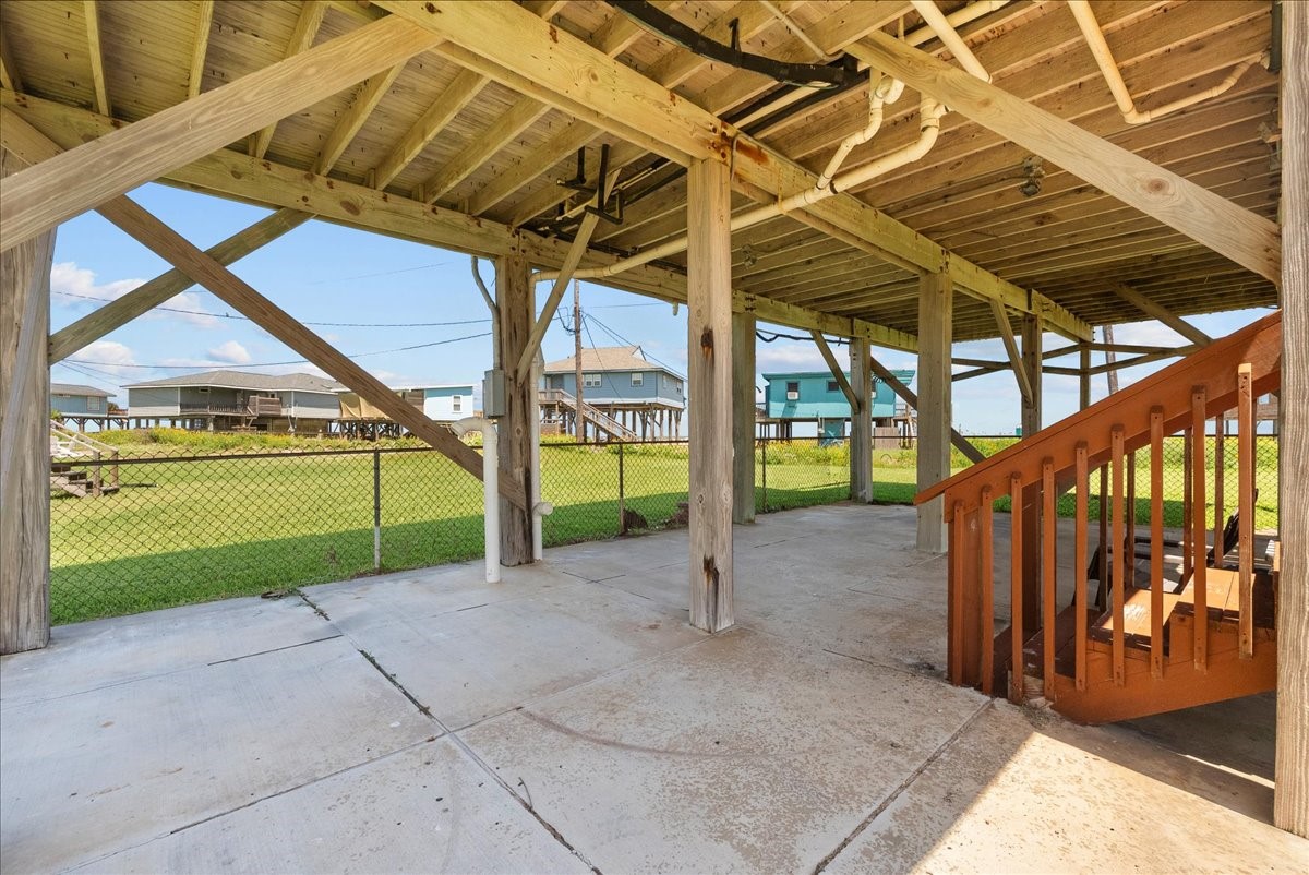 819 Seashell Drive Surfside Beach, TX 77541 - Photo 28 of 36 This photo shows a covered outdoor area under a raised house with wooden supports and a concrete floor. There are stairs leading up, and a fenced grassy yard is visible, offering space for outdoor activities.