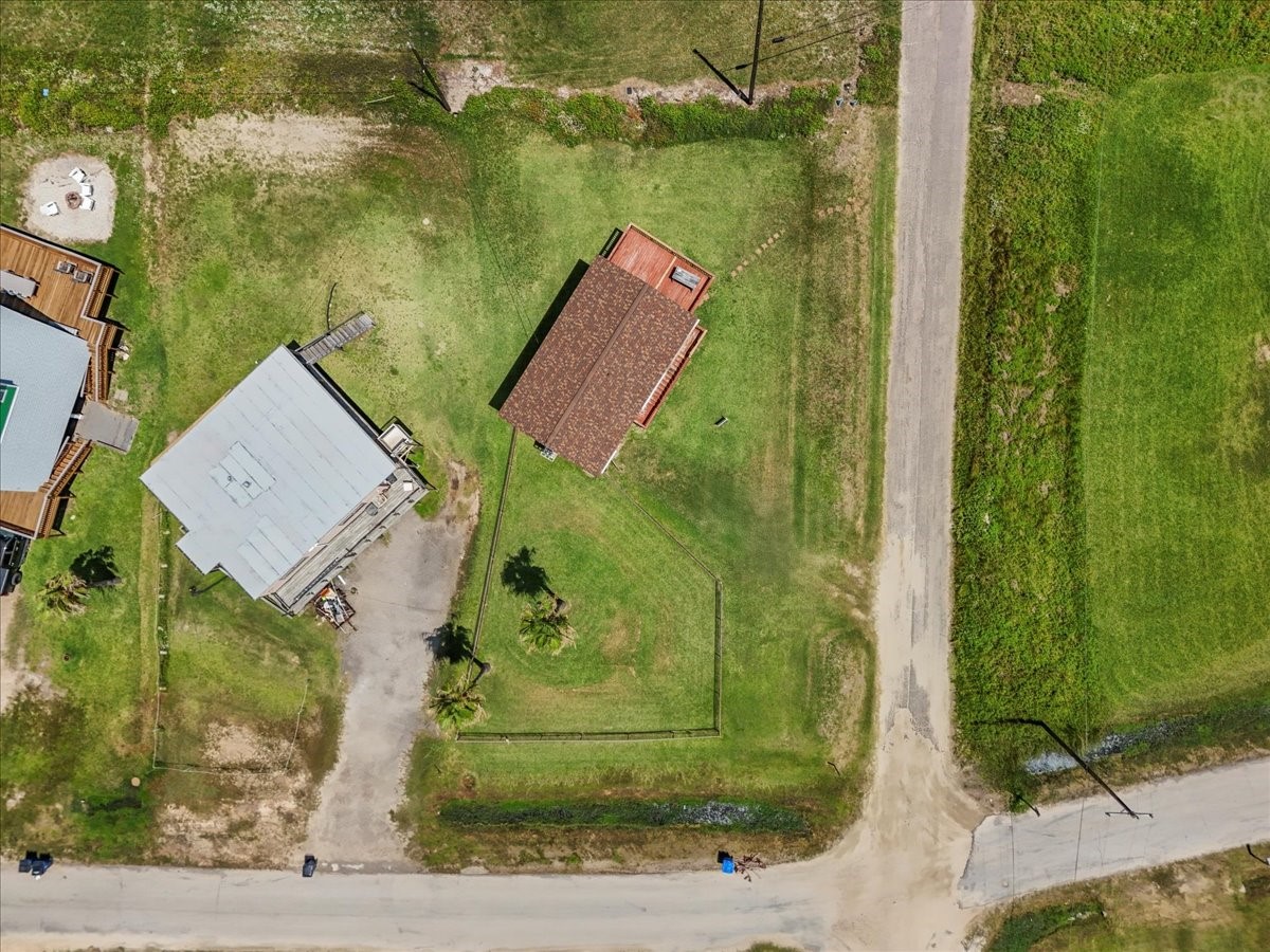 819 Seashell Drive Surfside Beach, TX 77541 - Photo 29 of 36 This aerial view shows a property with a house featuring a brown roof and spacious yard. It is located at a corner with two roads and is adjacent to another home. The area is predominantly green with open spaces, providing a sense of privacy and ample outdoor space.